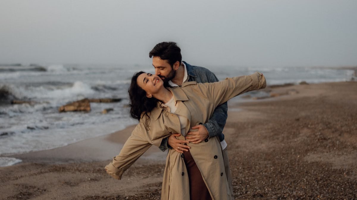A loving couple shares a tender embrace on a serene beach, capturing a moment of happiness.